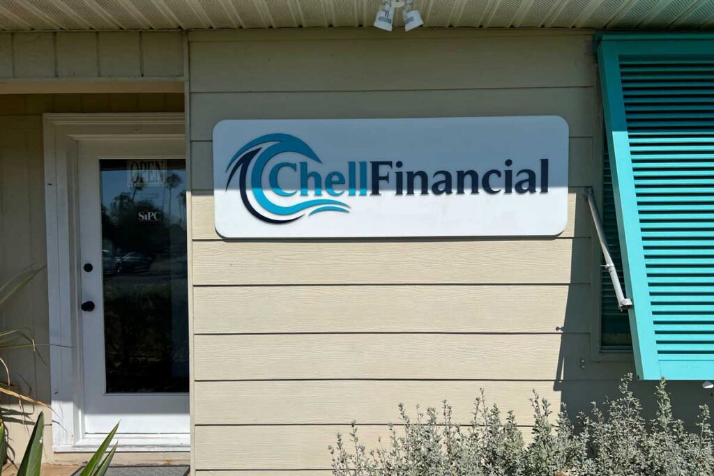A sign reading "Chell Financial" is mounted on the exterior wall of a beige building next to a door and a turquoise window shutter.