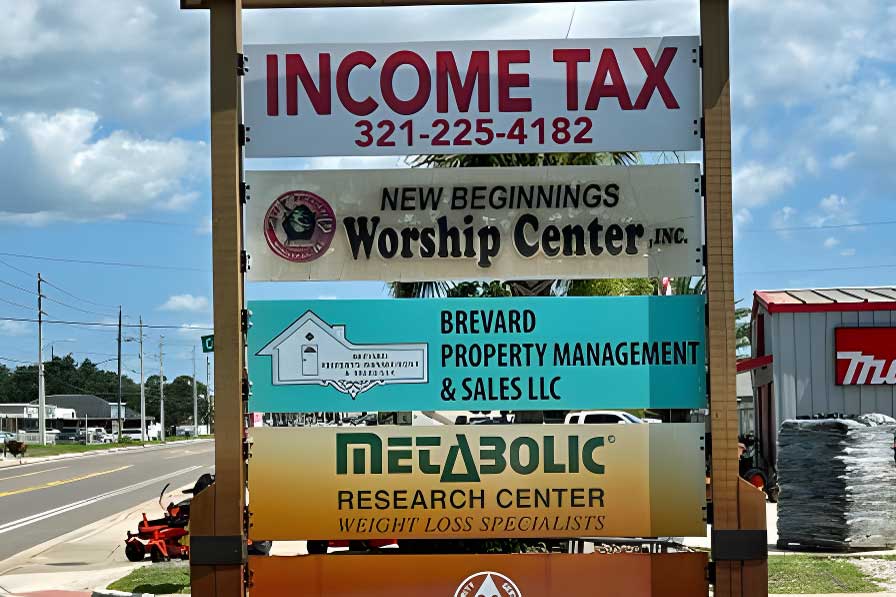 A roadside sign displays four businesses: Income Tax, New Beginnings Worship Center, Brevard Property Management & Sales LLC, and Metabolic Research Center.