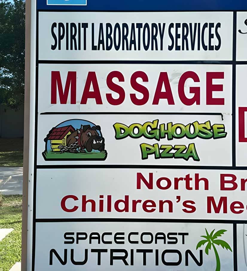 A sign displays advertisements for multiple businesses, including Spirit Laboratory Services, Massage, Doghouse Pizza, North Brevard Children’s Medical Center, and Space Coast Nutrition.