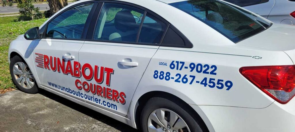 White sedan with "Runabout Couriers" logo and website on the side, along with two phone numbers printed in blue text on the rear door.