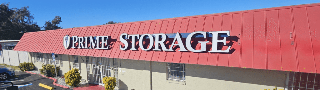 A beige building with a red roof displays a large “Prime Storage” sign in white letters above several barred windows.