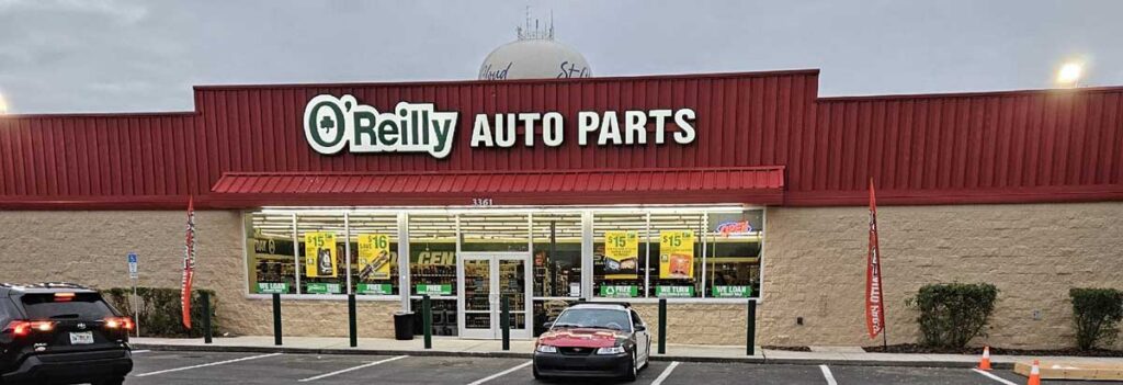O’Reilly Auto Parts store with a red roof, large sign, parked cars in front, and promotional posters on the windows.