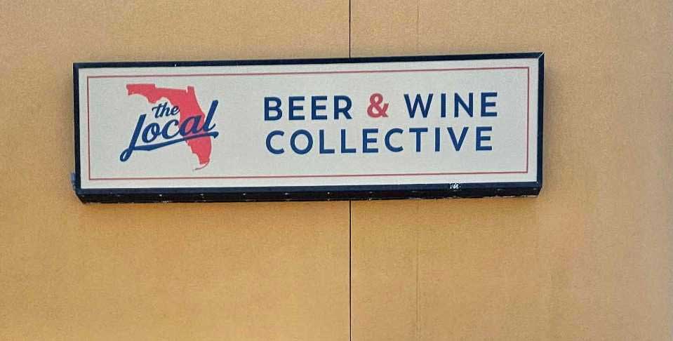 Rectangular sign reads “The Local Beer & Wine Collective” with a red Florida state outline on a beige wall.